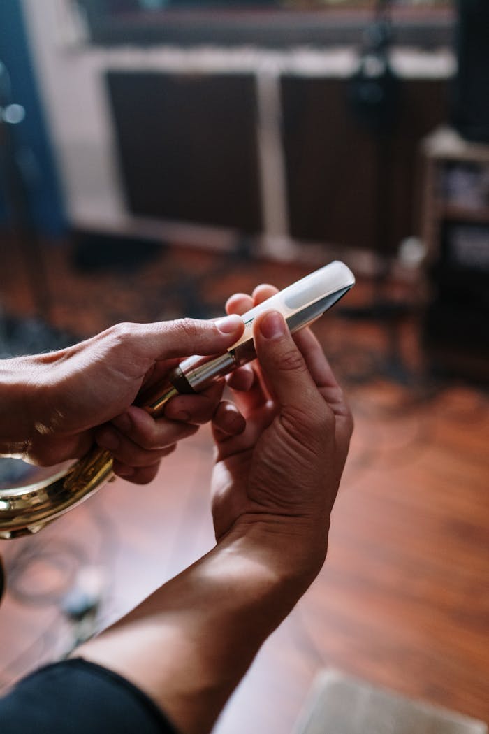 Close-up of hands fitting a mouthpiece on a saxophone indoors in a studio.